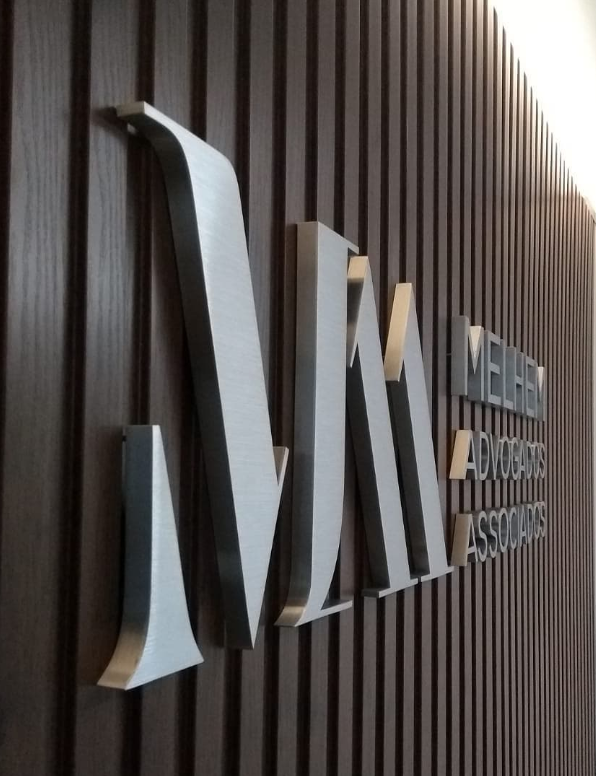 Letras caixa pretas instaladas sobre painel de ripado de madeira em lobby corporativo de alto padrão