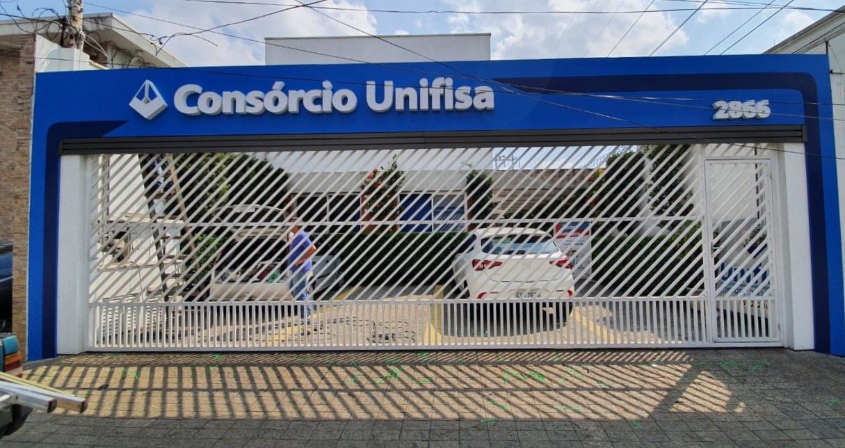 Letras caixa brancas Consórcio Unifisa em fachada azul com portão de grade branco