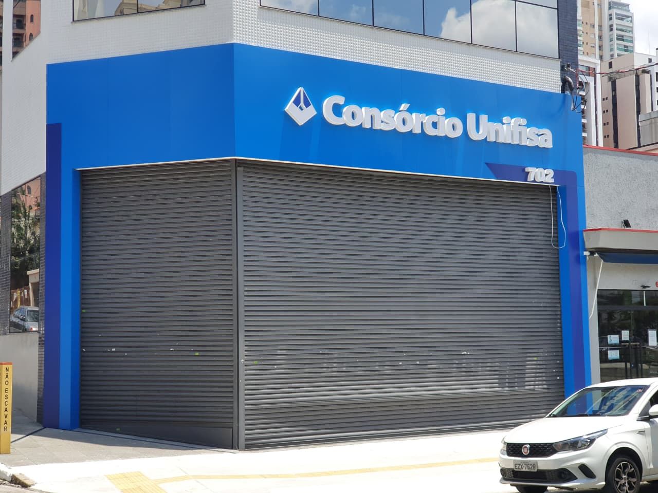 Letras caixa brancas Consórcio Unifisa instaladas em fachada azul de esquina com símbolo facetado
