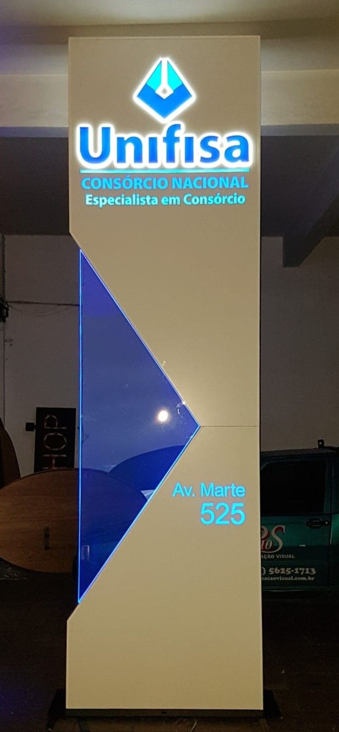 Totem vertical luminoso com letra caixa Unifisa em azul iluminado e acrílico azul facetado sobre estrutura branca